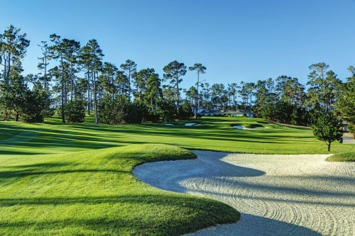 A scenic golf course with lush green fairways, sand traps, and tall trees under a clear blue sky.