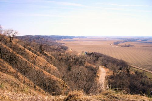 A scenic view of rolling hills and farmland under a clear blue sky, with a winding road through the landscape.