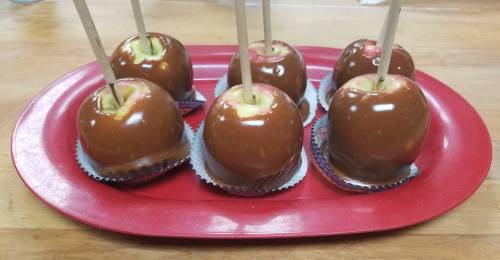 A red platter holds six caramel apples on sticks, each in a cupcake liner.