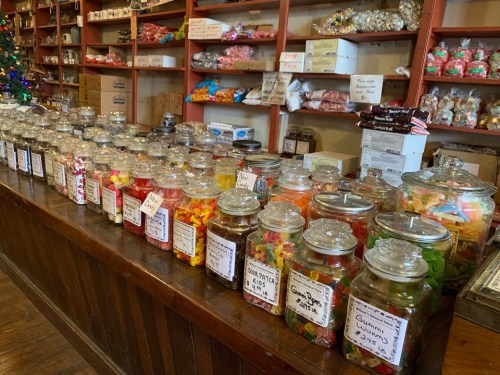 A colorful display of jars filled with various candies on a wooden counter in a cozy shop.