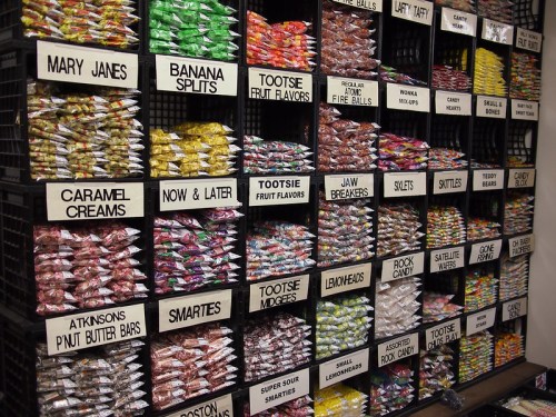 A colorful display of various candies in labeled bins, including Mary Janes, Tootsie Rolls, and Smarties.