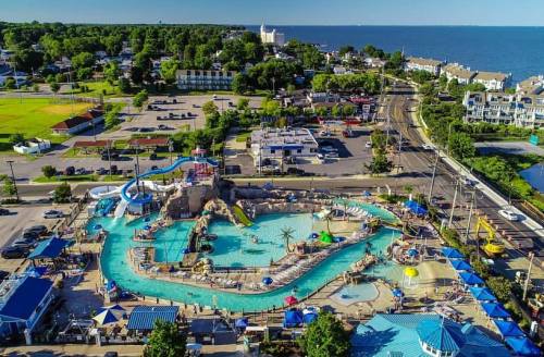 Aerial view of a vibrant water park with slides, pools, and surrounding greenery near a lake.