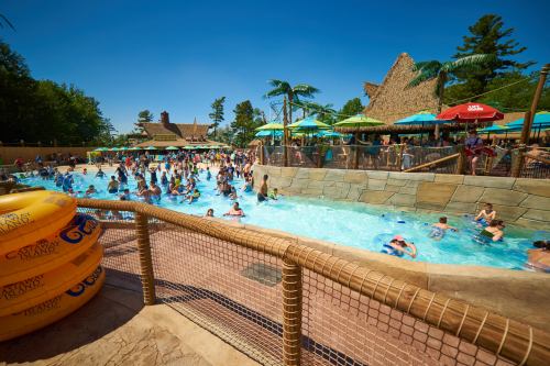 A busy water park scene with people swimming, lounging, and enjoying the sun around a large pool with tropical decor.