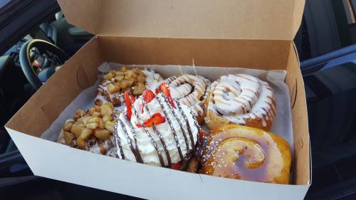A box of assorted pastries, including cinnamon rolls, a fruit-topped dessert, and a glazed donut.