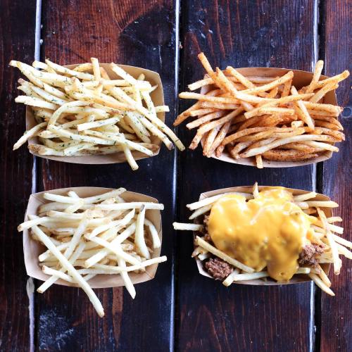 Four boxes of fries on a wooden table: plain, seasoned, spicy, and topped with cheese.