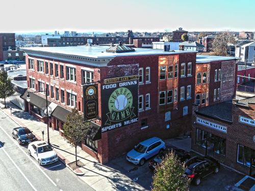 Aerial view of a brick building with a large sign for food, drinks, and sports music, surrounded by parked cars.