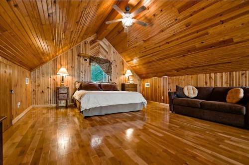 Cozy wooden bedroom with a sloped ceiling, a bed, a sofa, and warm lighting.
