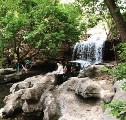 A serene waterfall surrounded by lush greenery, with people exploring the rocky area nearby.