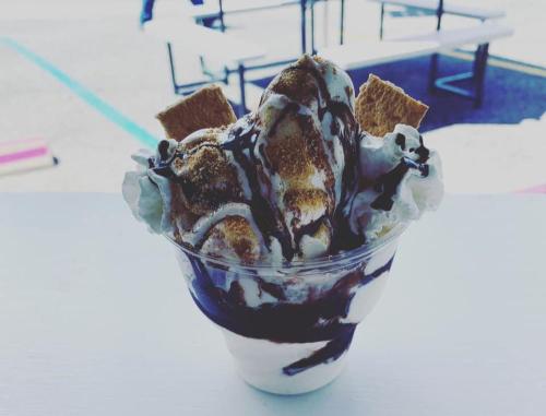 A delicious ice cream sundae topped with whipped cream, chocolate drizzle, and graham cracker pieces in a clear cup.