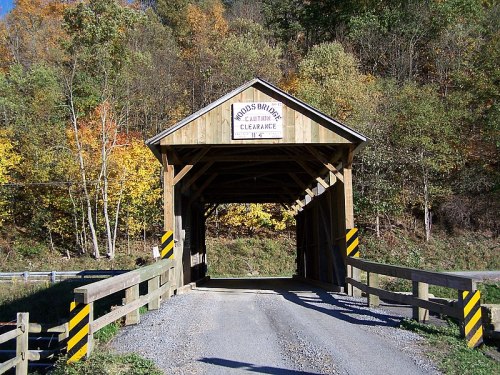 A wooden covered bridge with a sign, surrounded by trees displaying autumn colors.