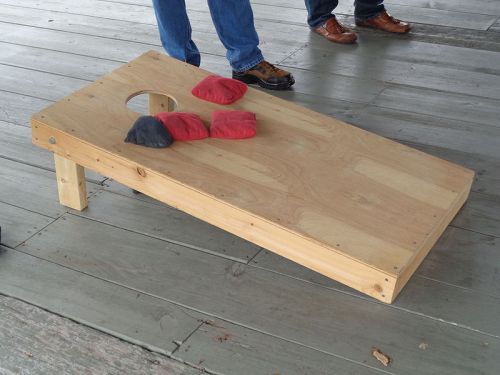 A wooden cornhole board with red and black bags on it, set on a wooden floor.