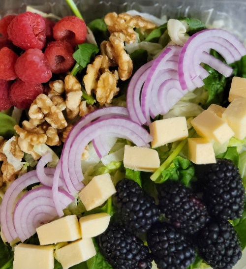 A colorful salad with spinach, raspberries, blackberries, walnuts, red onion, and cheese cubes.