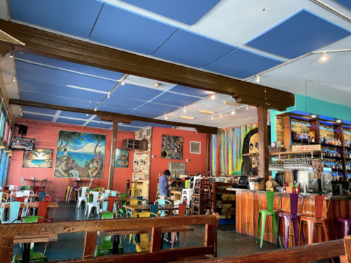 Colorful restaurant interior with vibrant murals, wooden beams, and eclectic seating arrangements.