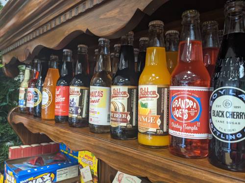 A wooden shelf displaying various colorful soda bottles, including brands like Grandpa Joe's and Jamaica's Finest.