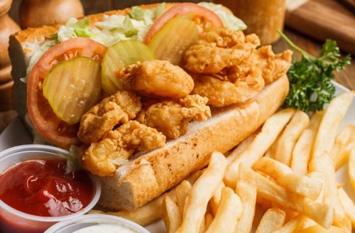 A crispy chicken sandwich with lettuce, tomatoes, and pickles, served with French fries and dipping sauces.