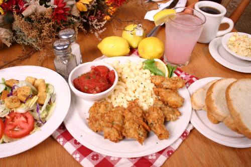 A plate of fried chicken, macaroni, and salsa, with a side salad, bread, and a drink on a wooden table.