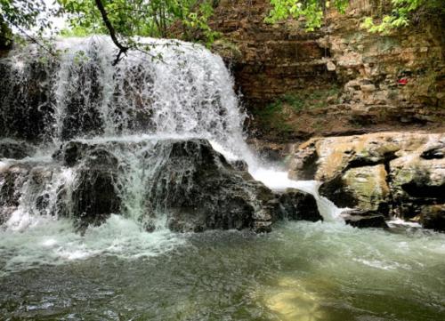 A serene waterfall cascading over rocky terrain, surrounded by lush greenery and a tranquil pool below.