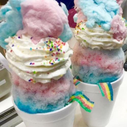 Two colorful ice cream cups topped with whipped cream, cotton candy, and rainbow sprinkles.
