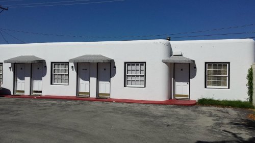 A row of white motel rooms with gray roofs and doors, set against a clear blue sky.