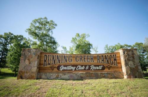 Sign for Running Creek Ranch Sporting Club & Resort, surrounded by greenery under a clear blue sky.