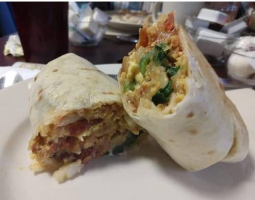 A close-up of a cut burrito filled with eggs, vegetables, and bacon, served on a plate.