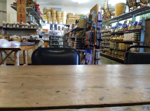 A rustic store interior with wooden shelves stocked with various goods, viewed from a table with empty chairs.