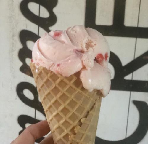 A hand holding a waffle cone filled with pink strawberry ice cream against a textured background.
