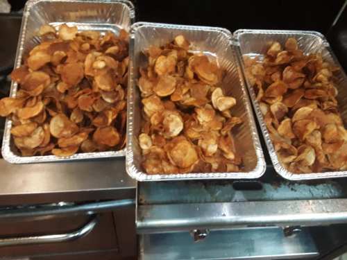 Three trays of golden-brown, crispy potato chips arranged neatly in aluminum containers.