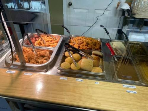 A buffet display with trays of fried chicken, cornbread, mashed potatoes, and brown gravy, behind a glass partition.