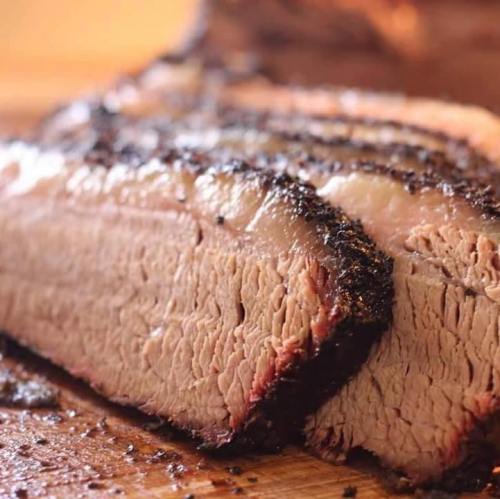 Close-up of a perfectly smoked brisket, showcasing its tender slices and smoky crust on a wooden cutting board.