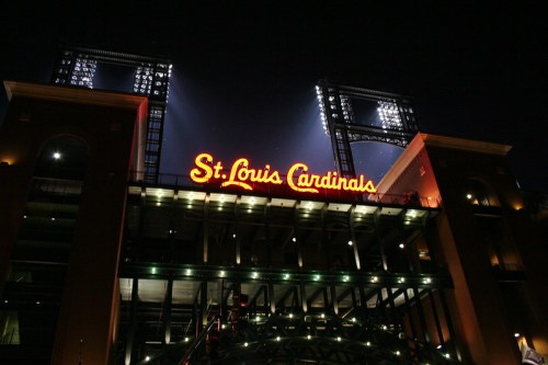 The illuminated entrance of the St. Louis Cardinals stadium at night, featuring the team's name in bright lights.