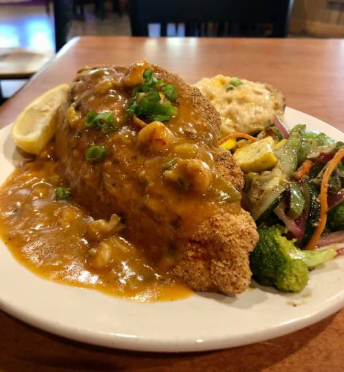 A plate featuring fried fish topped with a savory sauce, served with vegetables and a side of cheesy rice.