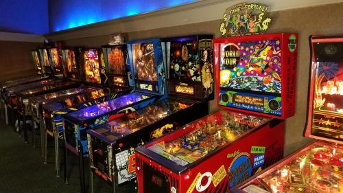 A row of colorful pinball machines illuminated in a dimly lit arcade setting.