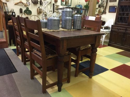 A rustic wooden dining table with four chairs, set in a colorful antique shop.