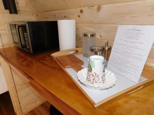 A wooden table with a microwave, paper towels, a coffee cup, and a menu in a cozy, wooden interior setting.
