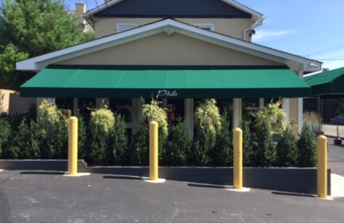 A building with a green awning and yellow poles, surrounded by greenery and a paved parking area.
