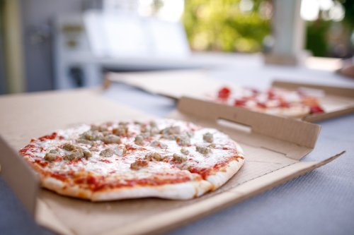 A close-up of a pizza with sausage on a cardboard box, with another pizza blurred in the background.
