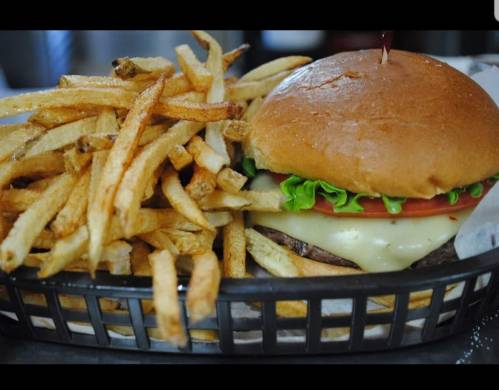 A juicy burger with cheese, lettuce, and tomato, served with a side of crispy French fries in a basket.