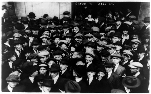A large crowd of people in hats gathered on Wall Street, capturing a moment from the early 20th century.