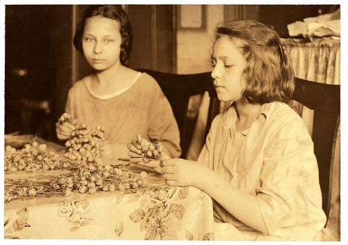 Two girls sit at a table, carefully arranging flowers, with a vintage atmosphere and soft lighting.