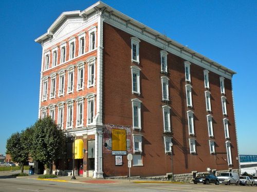Historic brick building with ornate detailing, featuring multiple windows and a clear blue sky in the background.