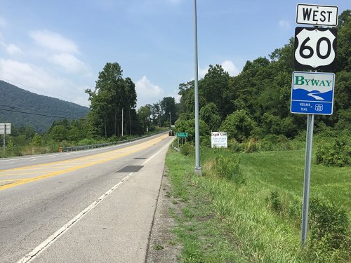A highway sign for West Route 60, with a scenic byway marker and green trees in the background.