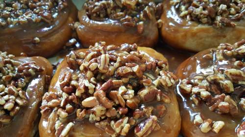 Close-up of sticky buns topped with caramel and chopped pecans, arranged in a tray.