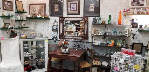 A cozy antique shop display featuring shelves of collectibles, a small table with chairs, and various decorative items.