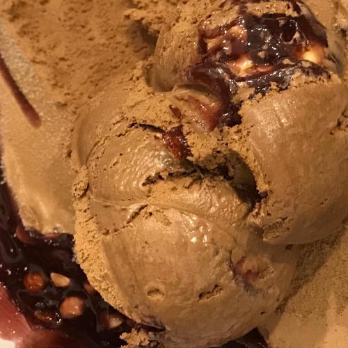 A close-up of a scoop of chocolate ice cream with a rich, glossy swirl of chocolate sauce on a textured surface.