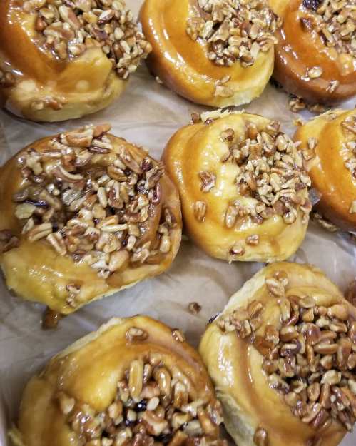 A close-up of sticky buns topped with caramel and chopped pecans, arranged on parchment paper.