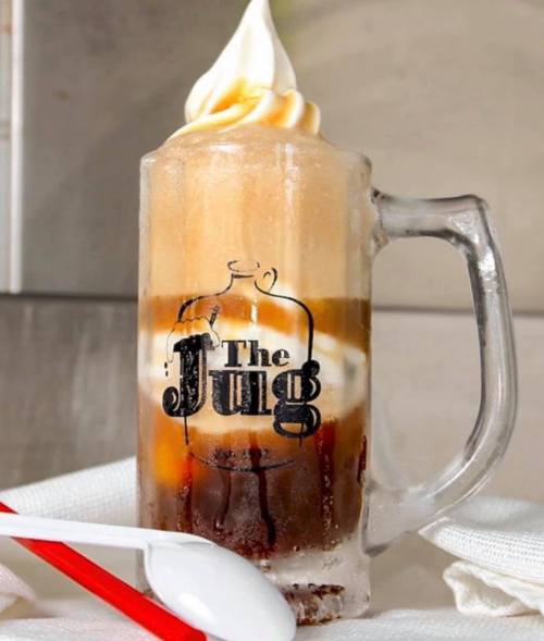 A frosty glass mug filled with layered ice cream and a dark beverage, topped with soft serve, featuring "The Jug" logo.