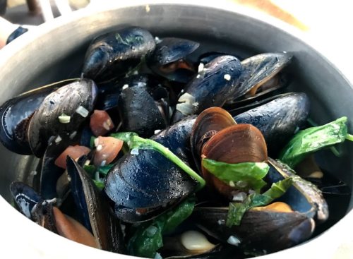 A close-up of cooked mussels in a pot, garnished with herbs and diced tomatoes.