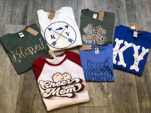 A collection of six t-shirts in various colors and designs, displayed on a wooden surface.