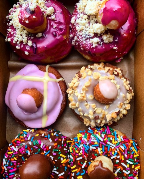 A box of colorful donuts with various toppings, including sprinkles, icing, and mini donuts on top.